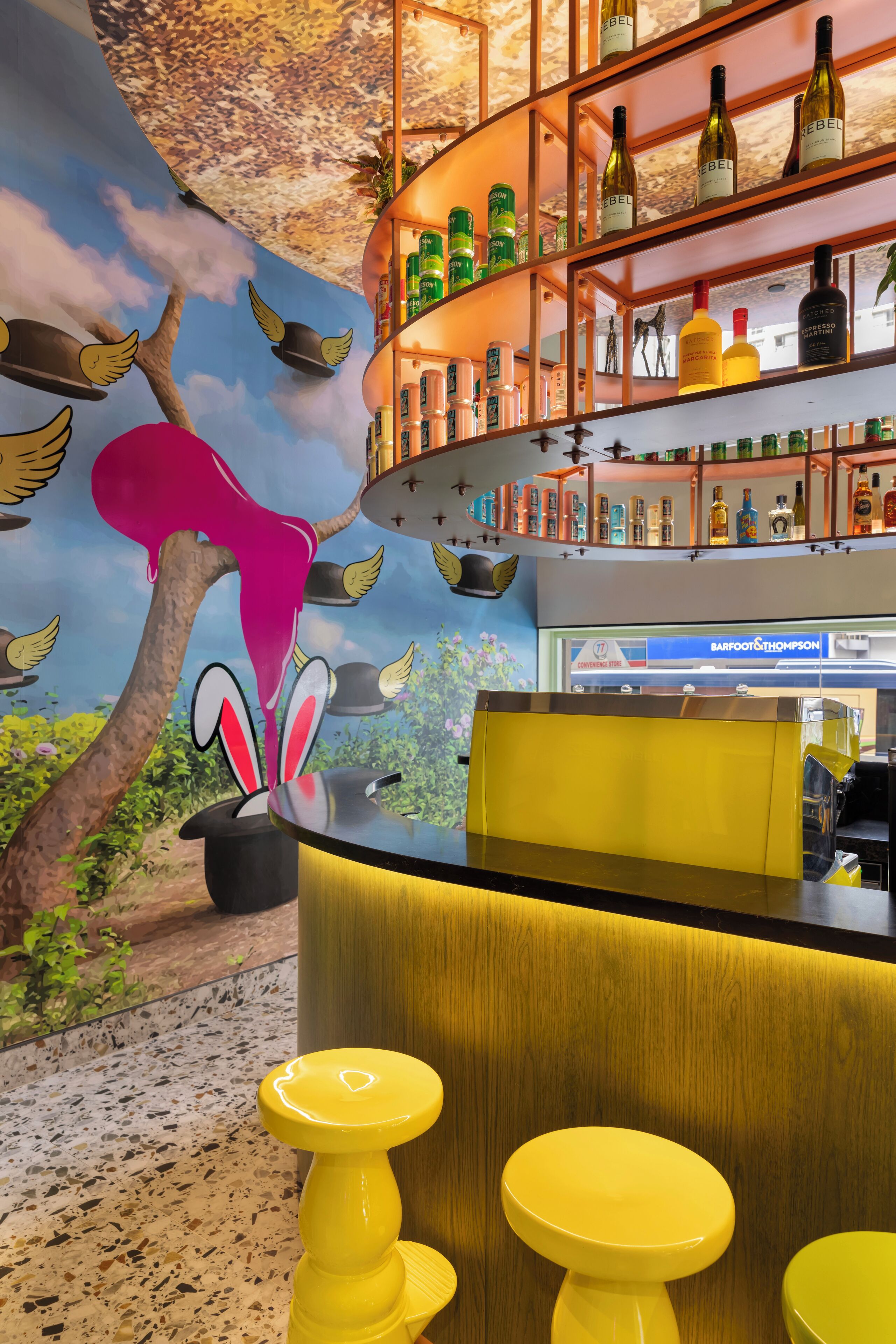 A bar area with a mural, shelves with bottles, and yellow stools.