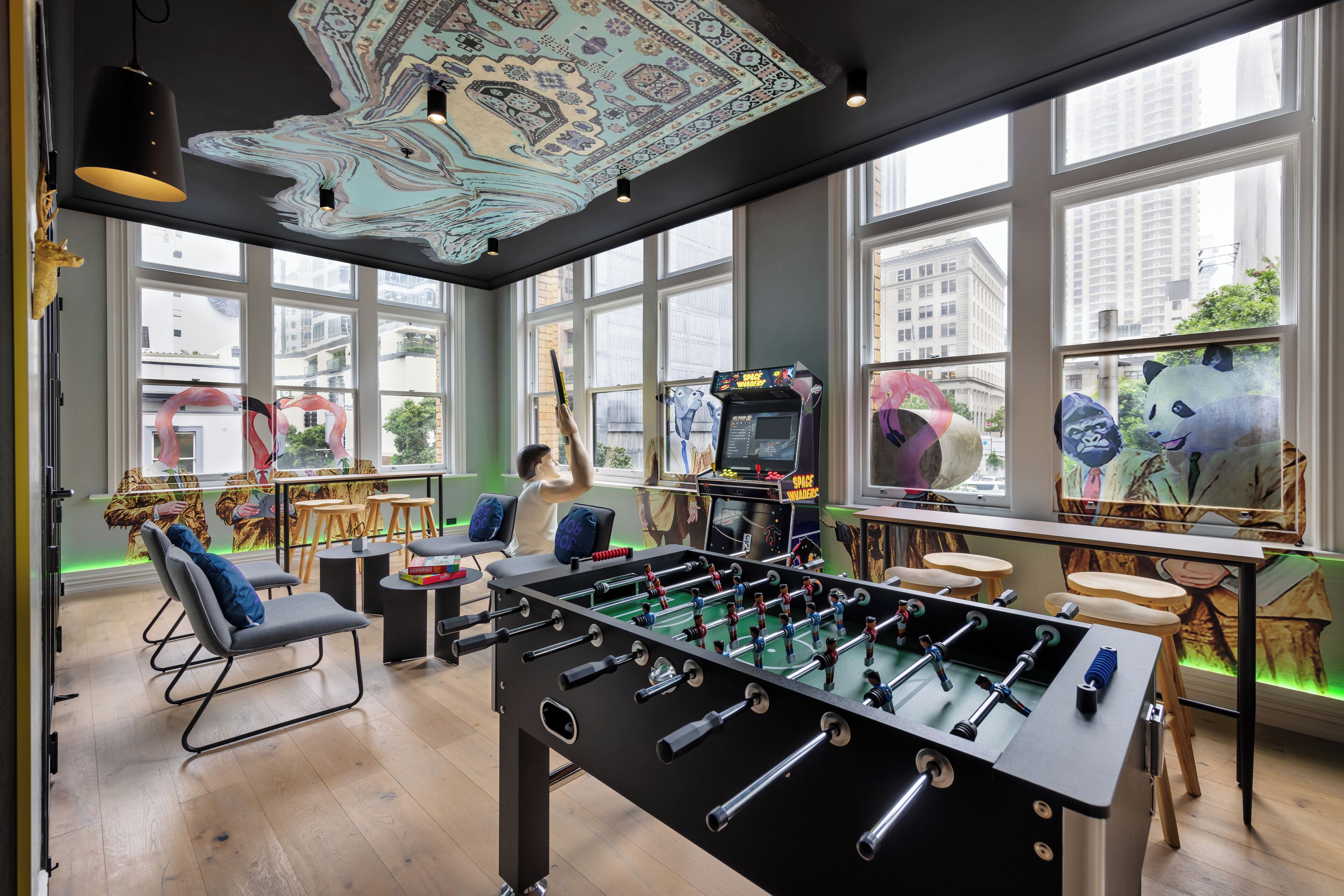 A room with a foosball table, comfortable seating, large windows, and a city view.