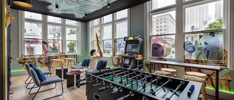 Una habitación con mesa de fútbol, asientos cómodos, ventanas amplias y vista panorámica de la ciudad.