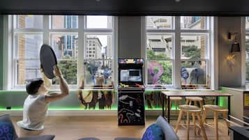 A room with arcade games, a large window with city views, and a table with stools.