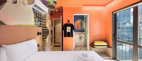 Una habitación de hotel con una cama grande, un baño con espejo y una maleta en un banco junto a la ventana.