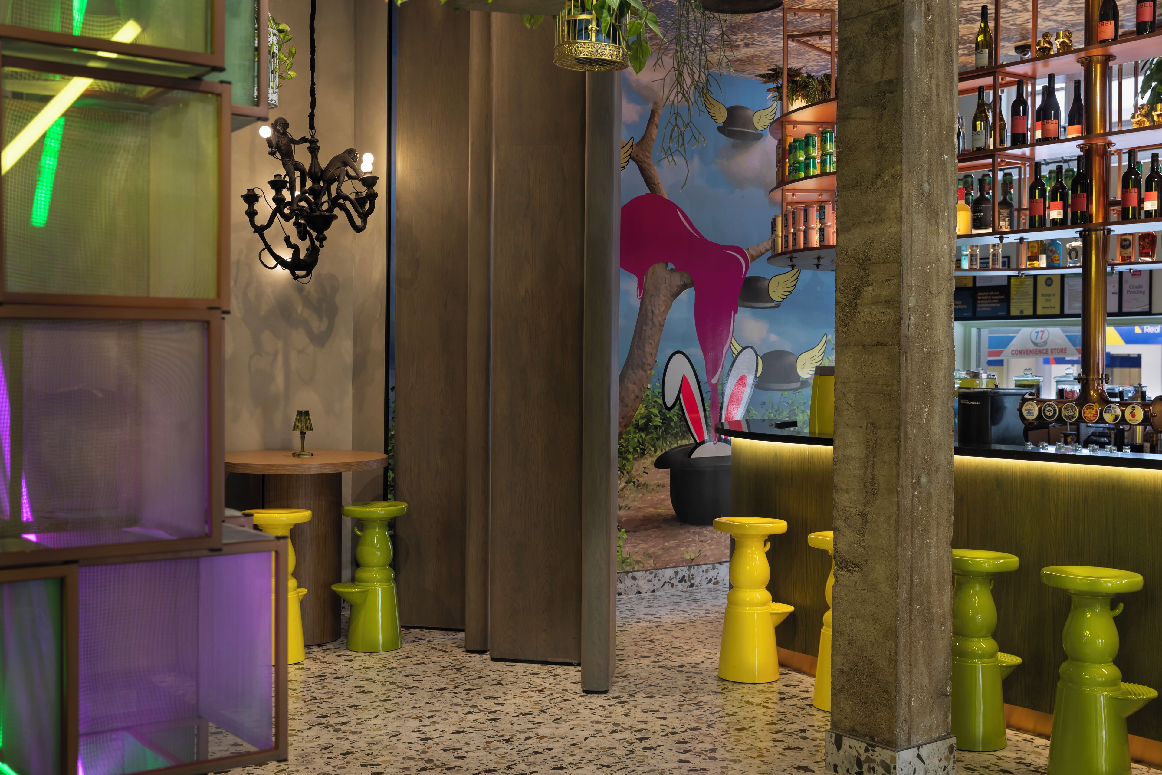 Uma área de bar com um mural, um candelabro e diversos frascos em prateleiras.