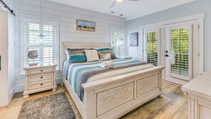 Une chambre à coucher comprenant un lit, une table de chevet, une commode, un ventilateur de plafond et une fenêtre avec des volets.