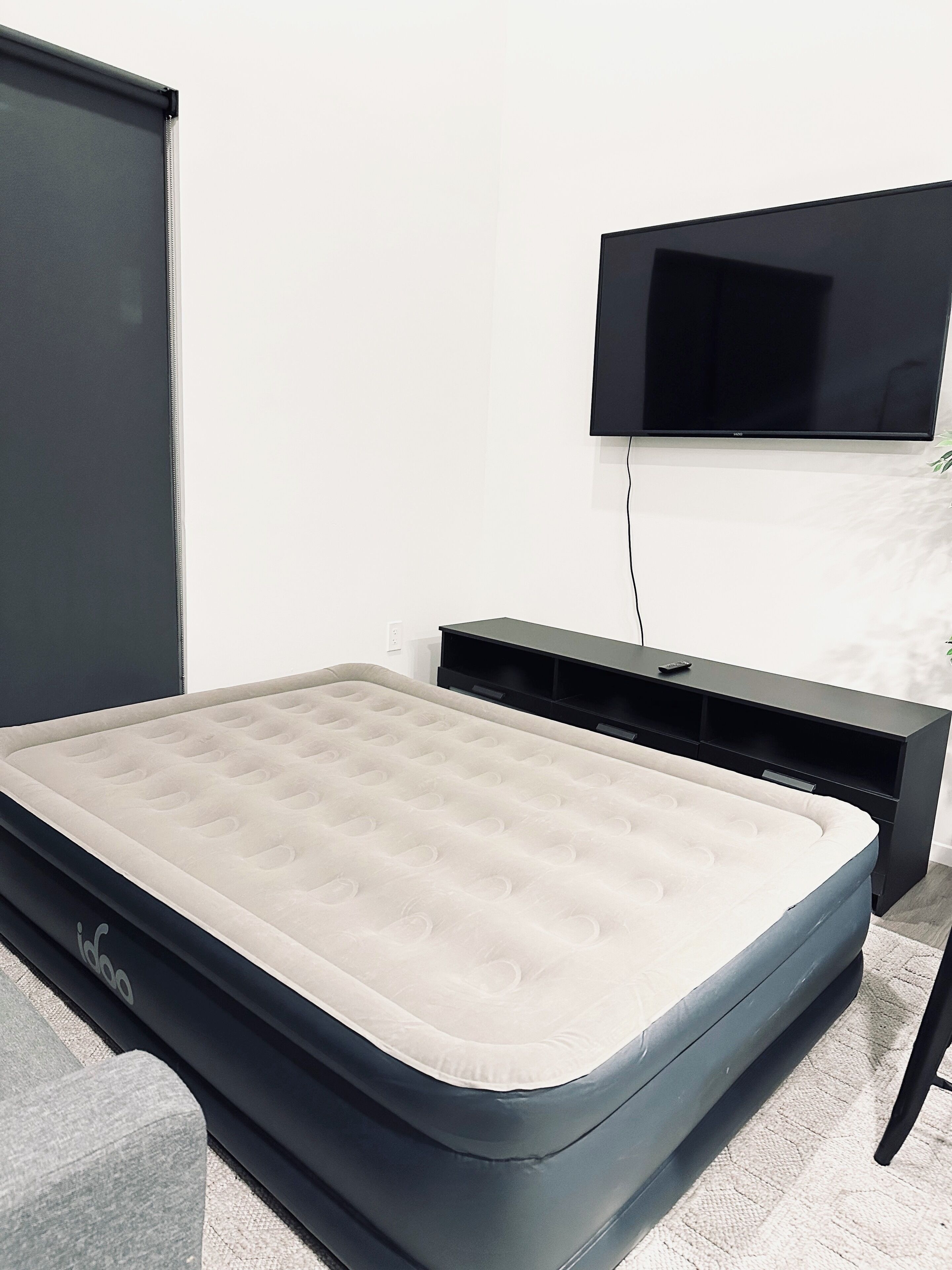 A bed with a mattress, a TV mounted on the wall, and a black entertainment unit.