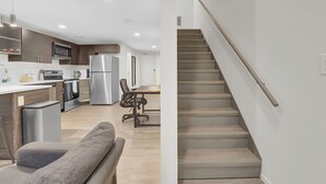 Une cuisine moderne équipée d’appareils électroménagers en acier inoxydable, un coin repas avec une table et des chaises, et un escalier doté d’une main courante.