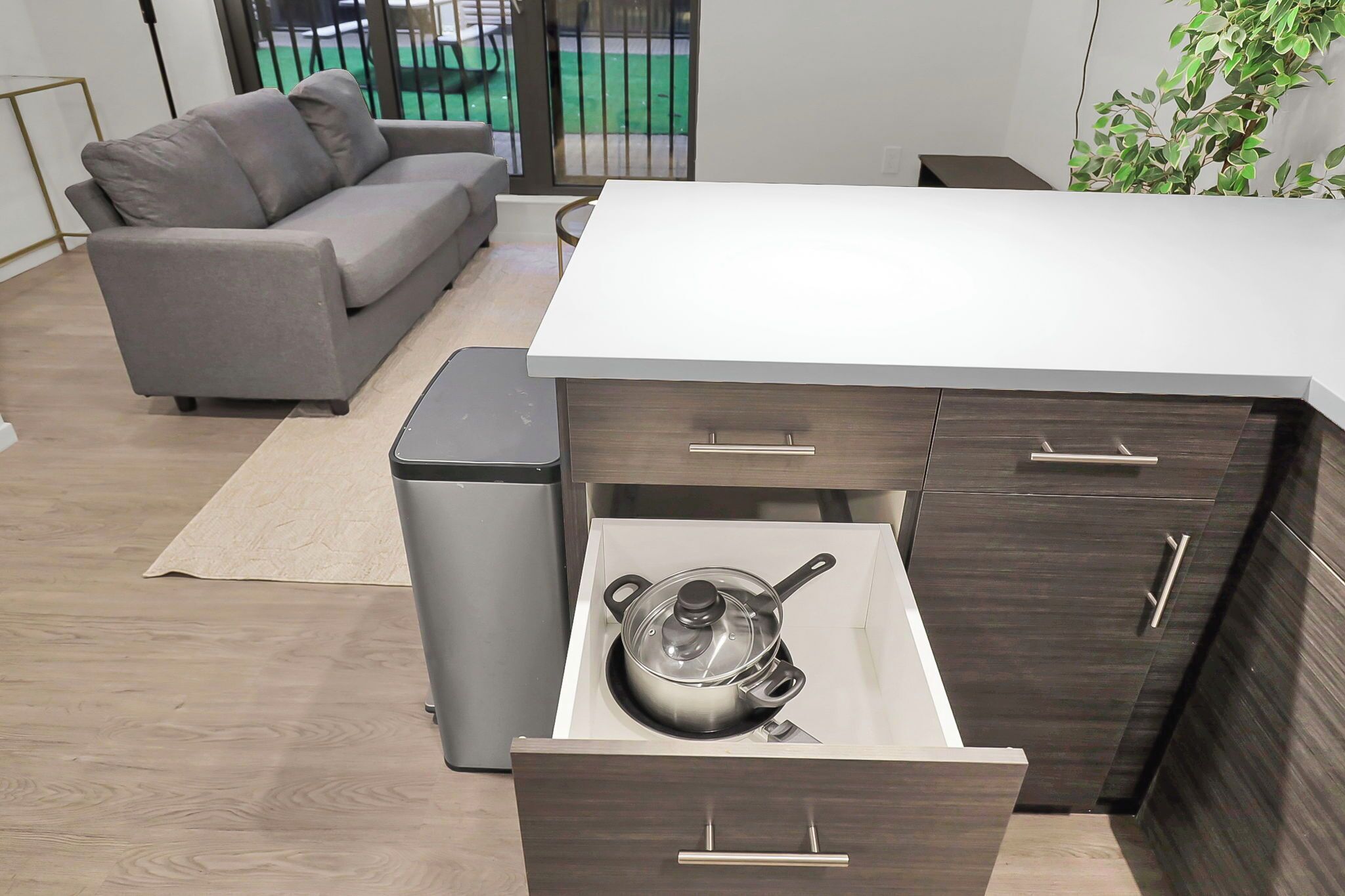 A modern kitchen with a built-in oven, a grey sofa, and a small dining table.