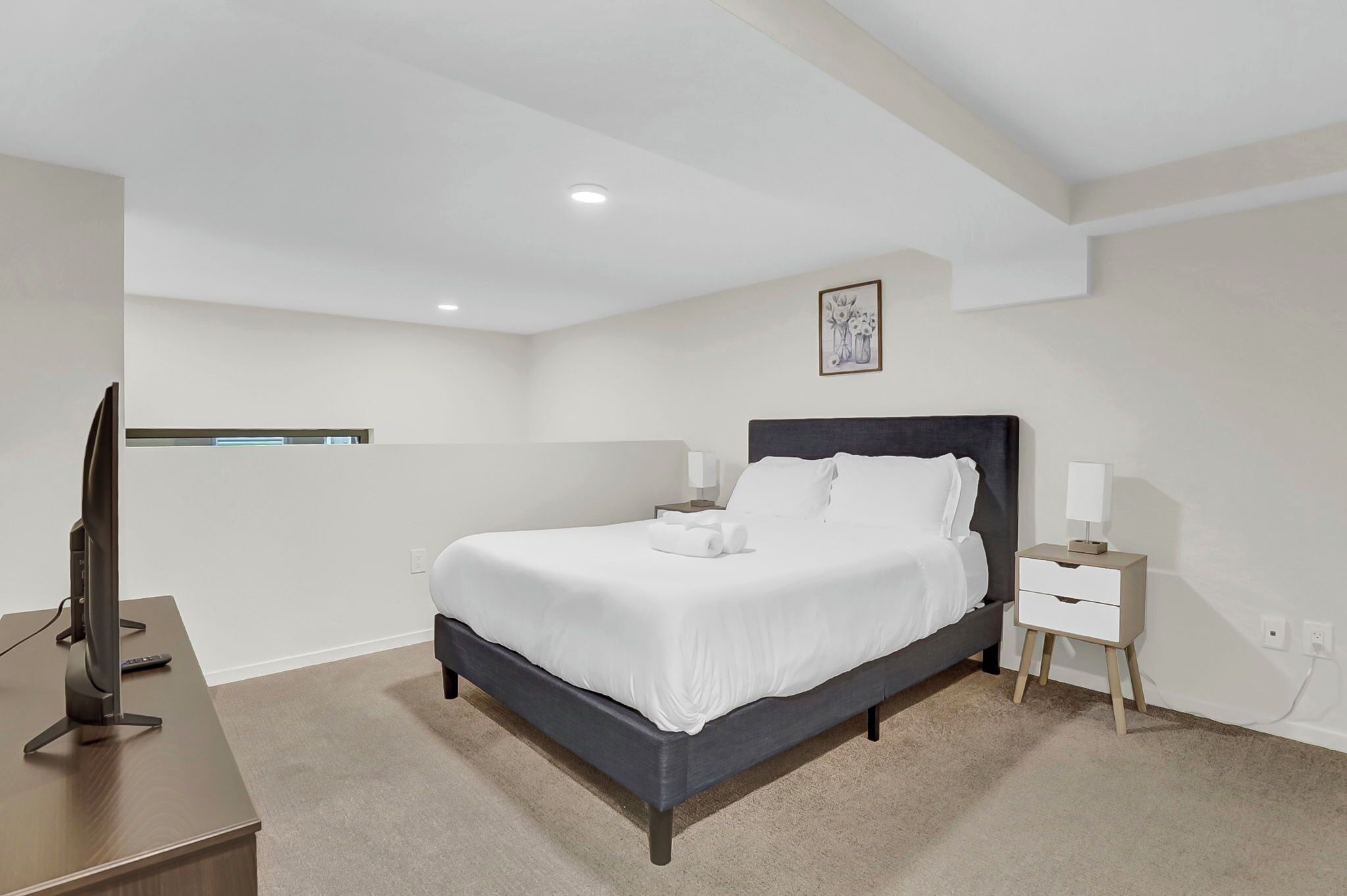 Une chambre à coucher avec un lit, une table de chevet, une lampe et un téléviseur posé sur un bureau.
