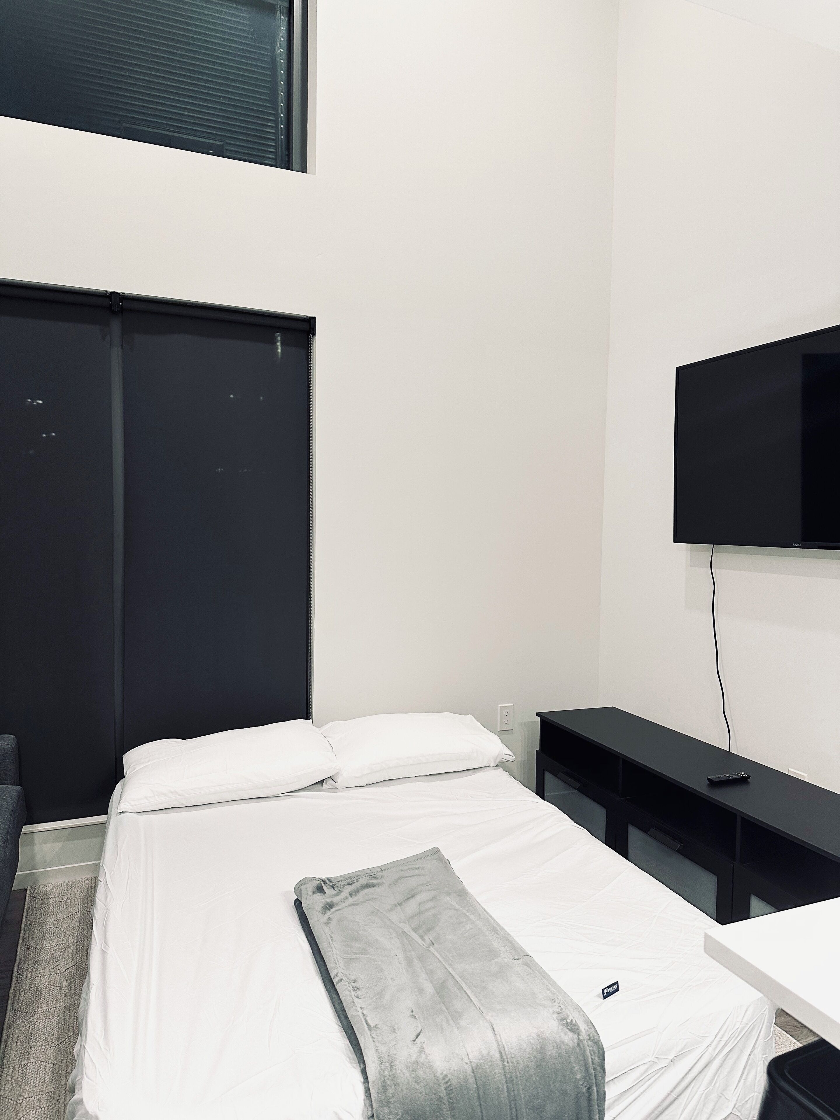 Een slaapkamer met een bed, een aan de muur bevestigde televisie, een bureau en een stoel.