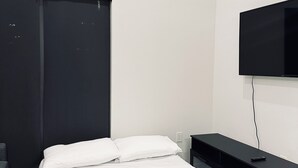 Une chambre à coucher avec un lit, un téléviseur fixé au mur, un bureau et une chaise.