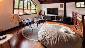 A spacious living room with a high ceiling, wooden beams, a large window, a television, and a bean bag. - Entire home in Florianópolis, Brazil near Lagoa, Mole and Joaquina (Lagoa da Conceição)