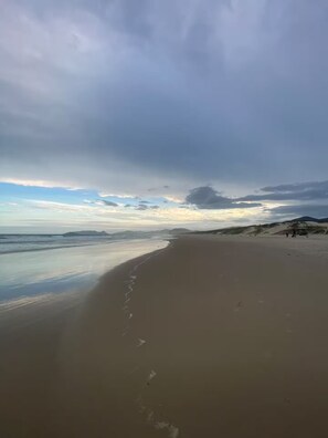Una spiaggia con un'ampia distesa sabbiosa, mare calmo e montagne lontane sotto un cielo nuvoloso.