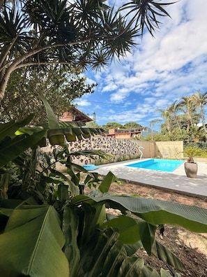 A swimming pool surrounded by lush greenery and a building with a patterned wall. - Entire home in Florianópolis, Brazil near Lagoa, Mole and Joaquina (Lagoa da Conceição)