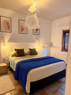 Une chambre à coucher comprenant un lit, une table de chevet, une commode, un luminaire suspendu et des œuvres d’art encadrées accrochées au mur.