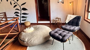 A room with a wooden floor, a large bean bag, a cushioned chair, a small table, and a hanging light fixture. - Entire home in Florianópolis, Brazil near Lagoa, Mole and Joaquina (Lagoa da Conceição)