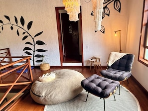 A room with a wooden floor, a large bean bag, a cushioned chair, a small table, and a hanging light fixture. - Entire home in Florianópolis, Brazil near Lagoa, Mole and Joaquina (Lagoa da Conceição)