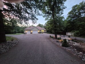 A two-story house with a driveway leading to a garage, surrounded by trees and a landscaped garden.