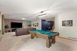 A living room with a pool table, a sofa, a television, and a staircase leading to another level. - The River House - 4 BR Retreat on the Apple River (Star Prairie)