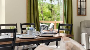 A dining table set for four with chairs, a view of greenery outside, and a window with curtains.