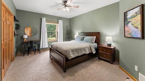 A bedroom with a bed, a desk, a chair, a ceiling fan, and a window with curtains.