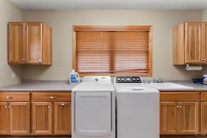 A laundry area with wooden cabinets, a washing machine, a dryer, and a window with blinds.