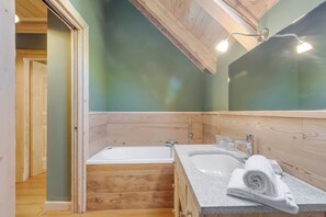 A wooden-paneled bathroom with a bathtub, a sink, and a mirror. - Baita Delle Stelle (Bessè Alto)