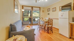 A cozy room with a sofa, dining table, chairs, and a kitchen area. - Appartamento Tracce Di Neve With Parking for 4 (Sestriere)