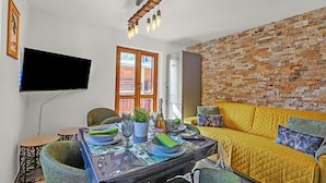 A modern living room with a brick wall, a yellow sofa, and a dining table set for four. - Appartamento Nube Di Argento Near Ski Lift (Sestriere)