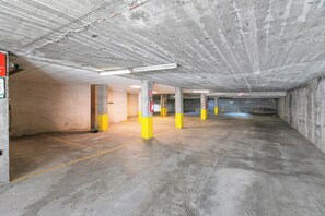 Un parking avec des piliers en béton, un éclairage fluorescent et un extincteur.