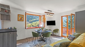 A modern living room with a dining area, large windows, and a flat-screen TV. - Appartamento Nube Di Argento Near Ski Lift (Sestriere)