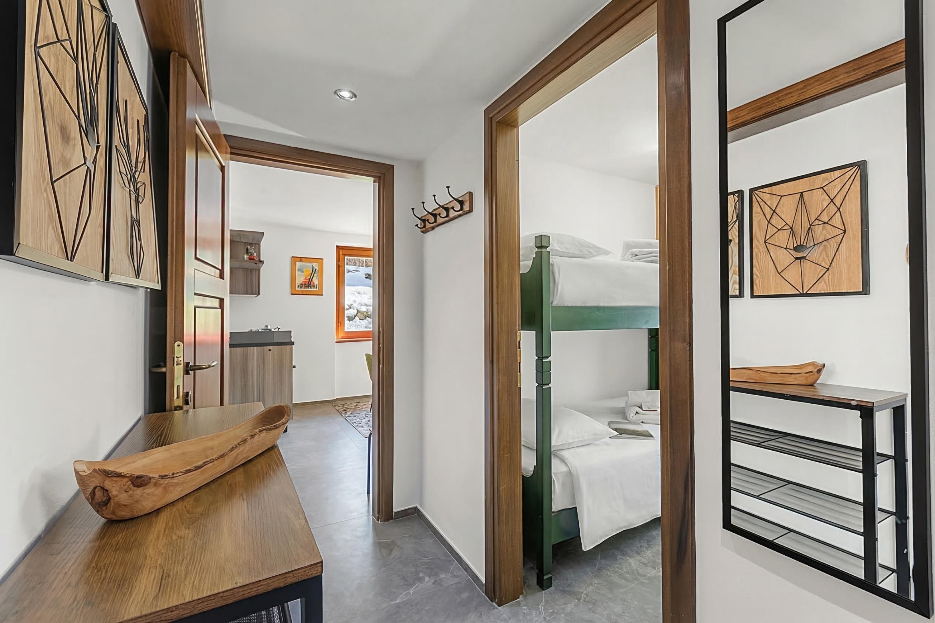 A hotel hallway with a wooden reception desk, a bunk bed room, and a wall-mounted coat rack.