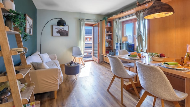A cozy living room with a sofa, a dining table with chairs, a bookshelf, and a large window with curtains. - Appartamento Alpine Suite Ski-in/out (Sestriere)