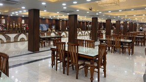 Eine geräumige Hotelhalle mit mehreren Esszimmertischen und Stühlen, edlen Kronleuchtern und einem polierten Marmorboden.