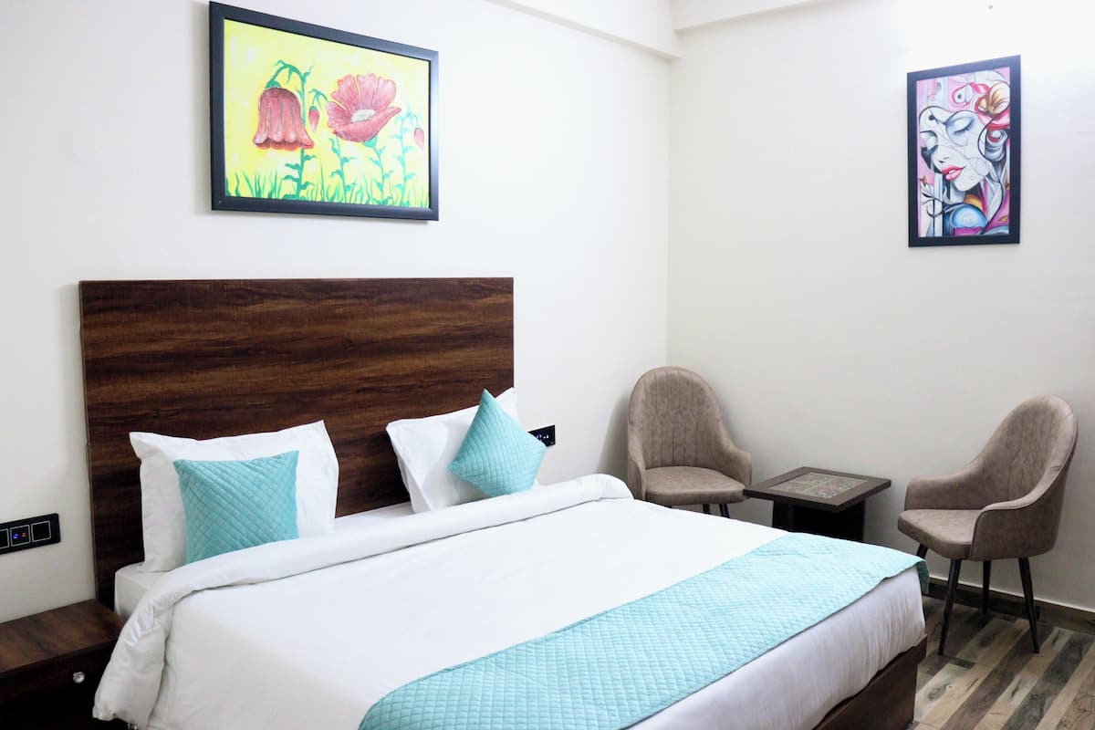 Een hotelkamer met een groot bed, twee stoelen, een tafeltje en twee schilderijen aan de muur.