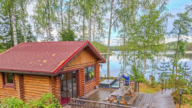 Une cabane en rondins dotée d’une terrasse et d’une porte vitrée, avec vue sur un lac.