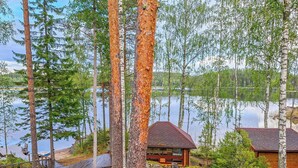 Une cabane dotée d’un toit en pente, entourée d’une forêt dense et bordée d’un lac.