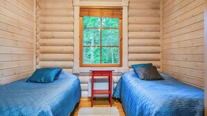 Quarto de cabana com duas camas, uma mesa pequena e uma janela com vista para o verde.