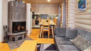 Interior acolhedor de uma cabana de madeira com lareira, mesa de jantar de madeira e um sofá cinzento.