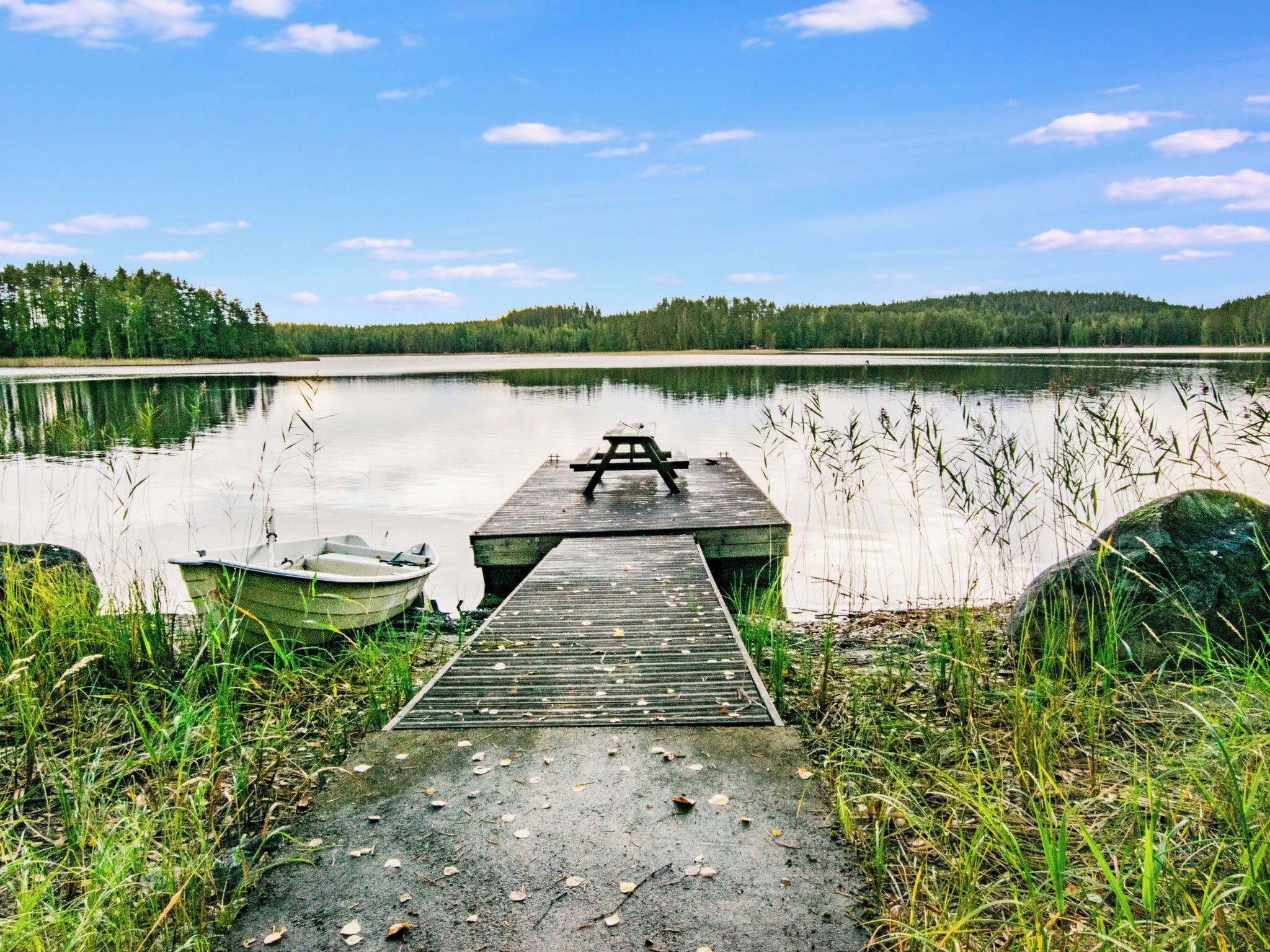 A wooden dock extending into a calm lake with a picnic table at the end.