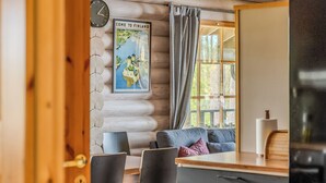 A cozy cabin interior with a wooden log wall, a dining area with a table and chairs, a sofa with cushions, and a large window with curtains. - Villa norppa by Interhome (Punkaharju)