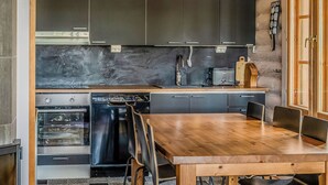 A compact kitchen with dark cabinets, a wooden dining table, and a built-in oven. - Villa norppa by Interhome (Punkaharju)