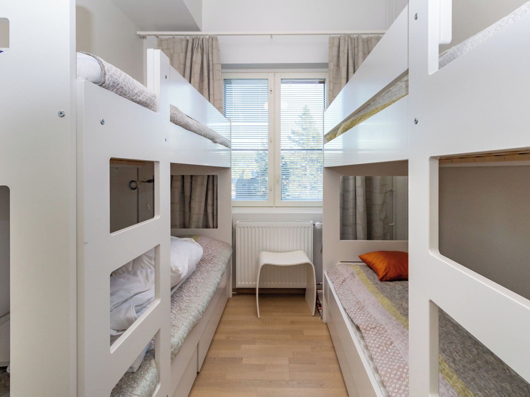 Una camera del dormitorio con letti a castello, un termosifone, una finestra con persiane e una sedia.