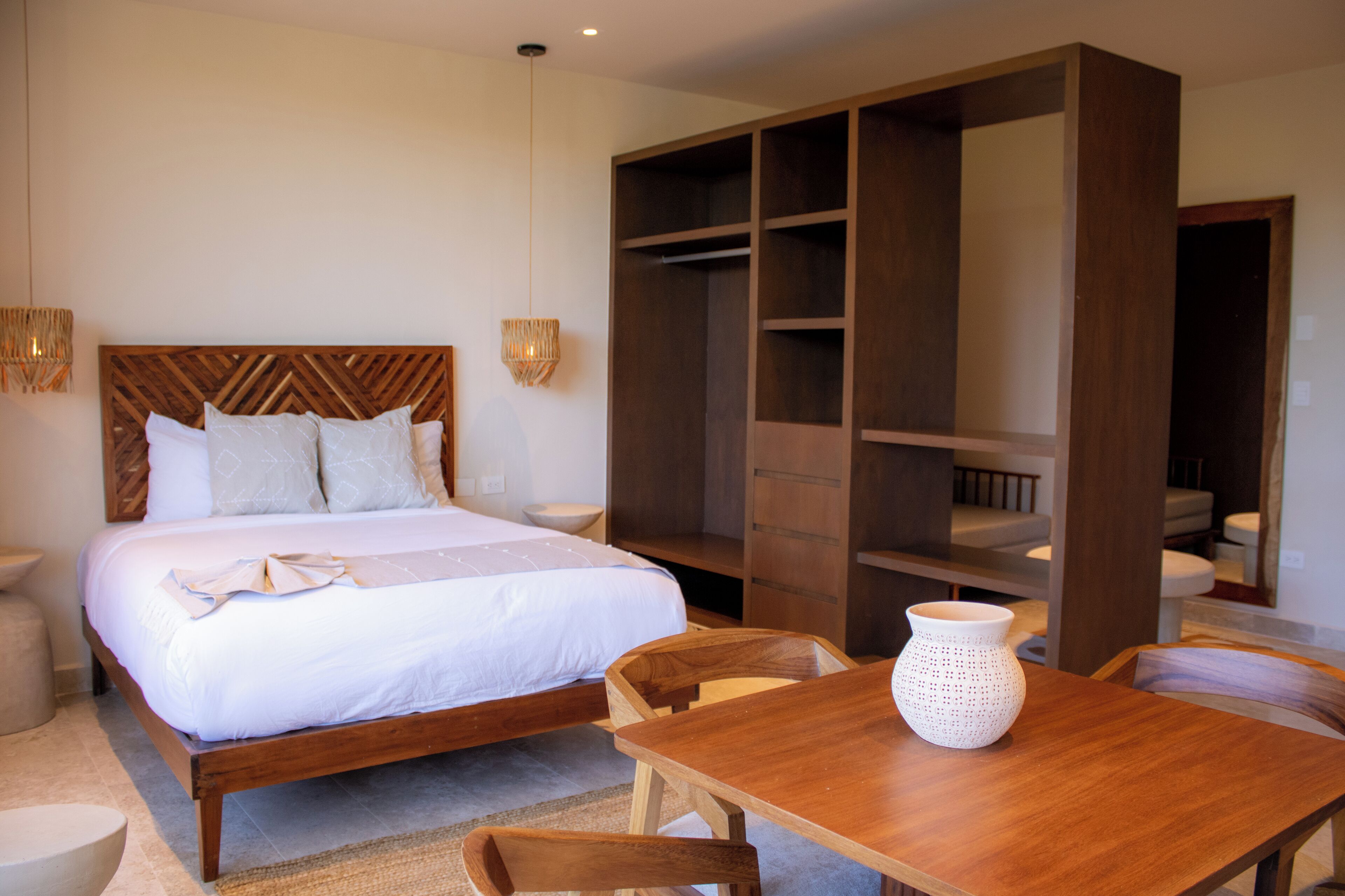 A bedroom with a wooden bed, a wooden wardrobe, a wooden table, and a white vase.
