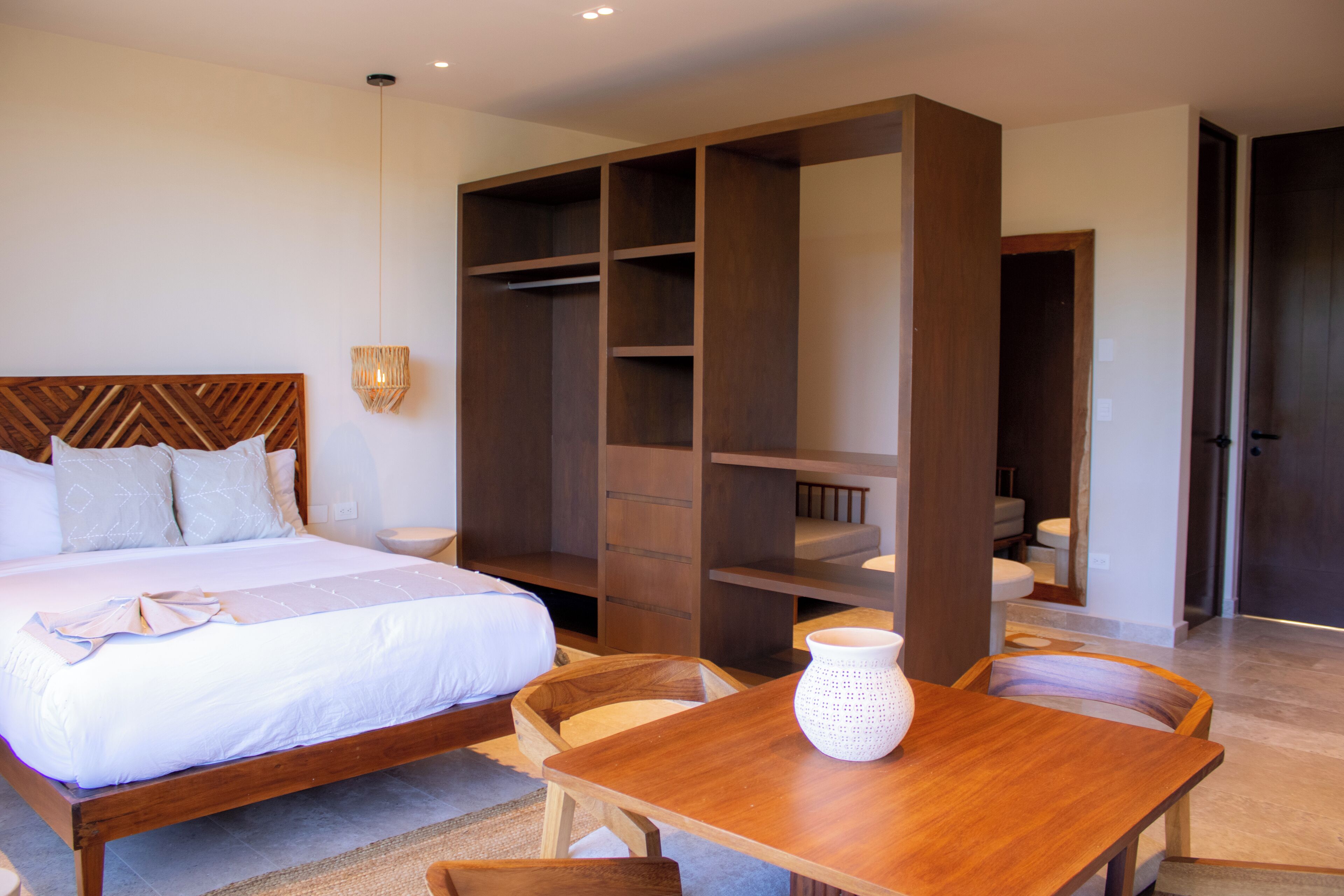 A bedroom with a wooden bed, a large wardrobe, a dining table with chairs, and a white vase.