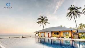 A hotel with a swimming pool, palm trees, and a view of the ocean. - Gerizim Hotel Resort (Chaung Thar)