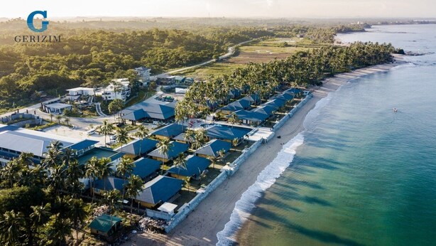 An aerial view of a coastal hotel with multiple blue-roofed buildings, a beachfront, and surrounding greenery. - Gerizim Hotel Resort (Chaung Thar)