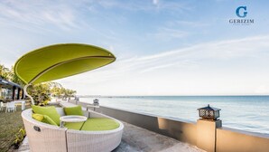 A wicker outdoor seating area with a green canopy, overlooking a calm sea. - Gerizim Hotel Resort (Chaung Thar)