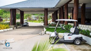 A golf cart parked in front of a building with a covered walkway and palm trees in the background. - Gerizim Hotel Resort (Chaung Thar)