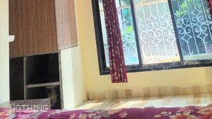 A room with a ceiling fan, a large window with decorative curtains, and a bed with a floral bedspread. - Mauli cottage (Murud)