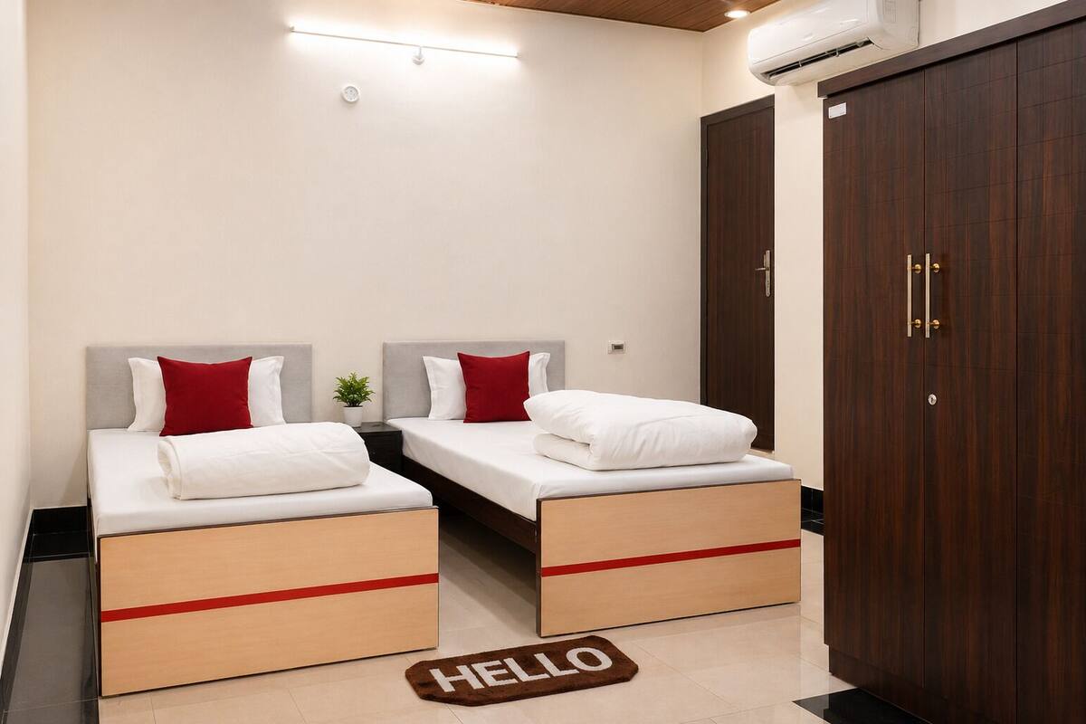 A double bed room with a wooden headboard, a red and white pillow, a small plant, and a 'HELLO' doormat.