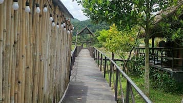 A wooden walkway with lanterns, leading to a thatched-roof structure.